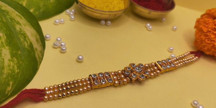Elegantly Designed Rakhi with a Golden Finish and Shiny Stones and Roli - Chawal